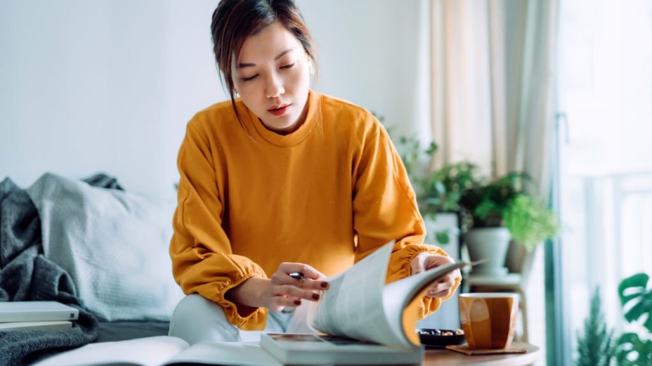 Focused young Asian woman reading book and making notes at home, concentrates on her studies. Further education concept